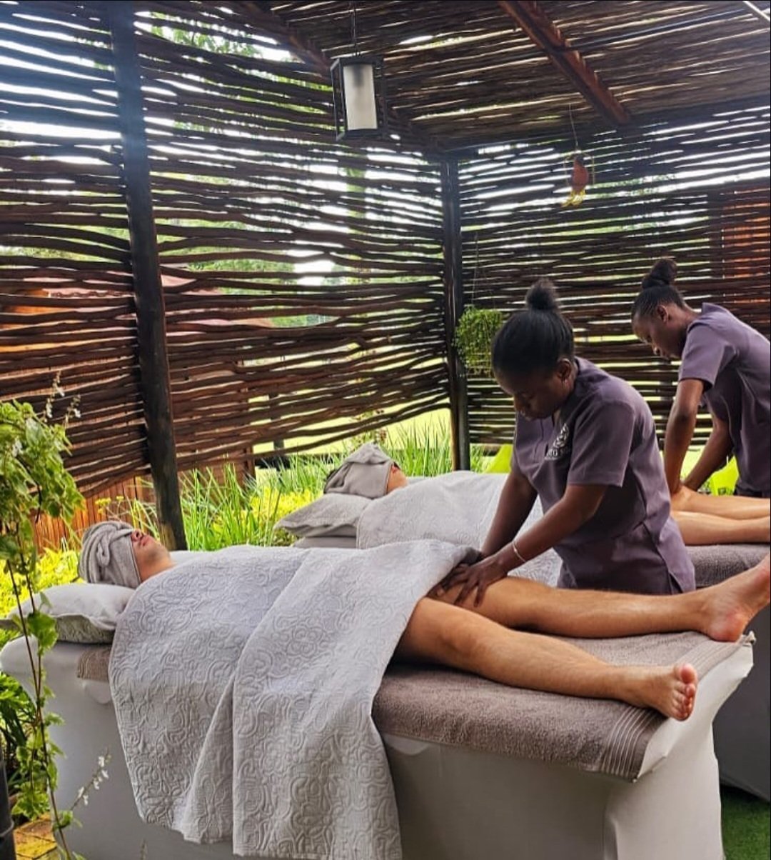 Two massage therapists providing treatment to a client in an outdoor spa setting with wooden lattice screens and potted plants