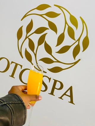 Hand holding a glass of beer in front of the OTG Spa logo with olive branch design on a white background