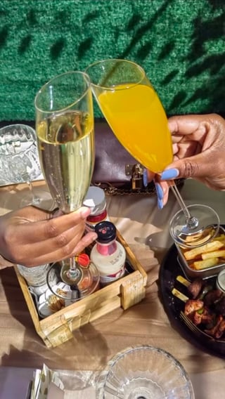 Person holding two glasses of champagne and orange juice with appetizers and a decorative green tablecloth background