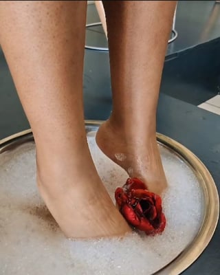 Persons legs soaking in a white bath with a red rose petal floating in the water