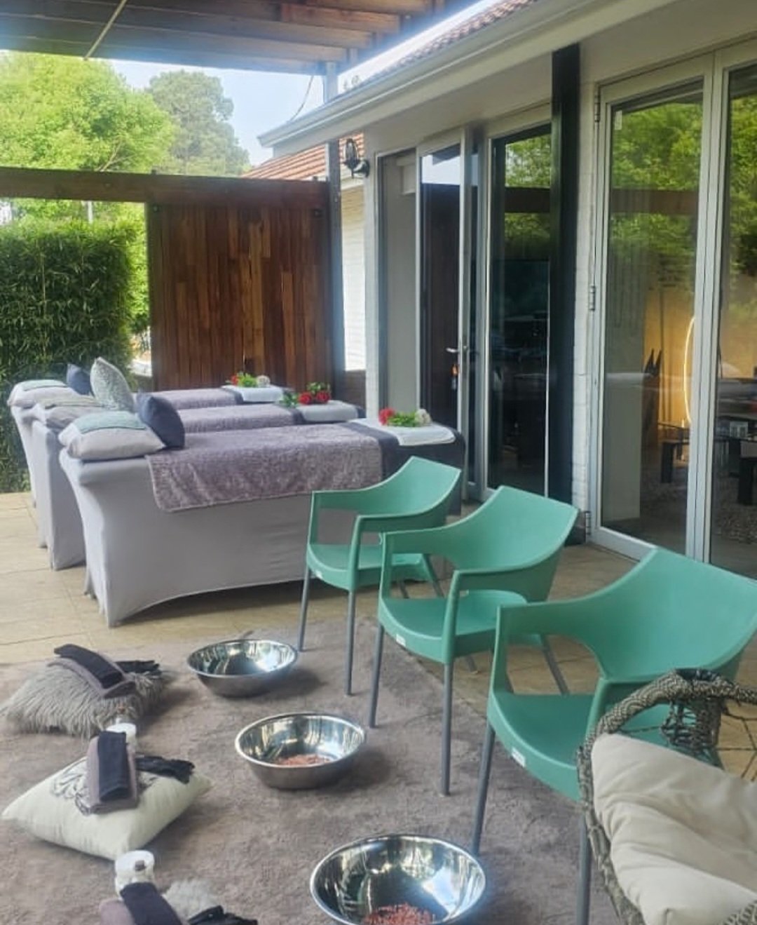 Modern patio with turquoise chairs, gray seating, metal bowls and a view of a house with large windows