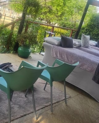 Two green modern chairs on a patio overlooking a garden with a gray sofa and vegetation in the background